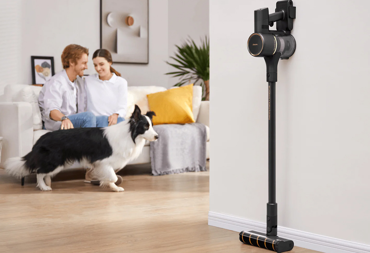 Απεικονίζεται η σκούπα στη βάση της στον τοίχο και δίπλα ένα ζευγάρι και ένας σκύλος στον καναπέ.